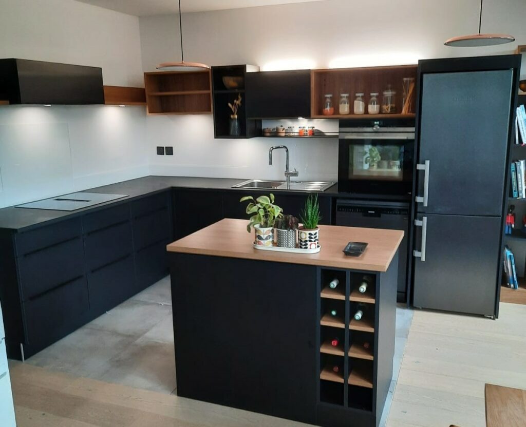 cuisine sur mesure, en anthracite mat, à l'exception d'un plan de travail, de quelques tablettes et caissons bois clair. Eclairages indirects dessus et dessous les meubles haut. Casiers pour bouteilles dans l'ilot central. Hotte encastrée dans la plaque de cuisson.
